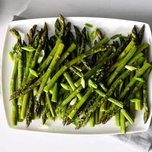 A person holding a pile of asparagus over a boiling pot of water.