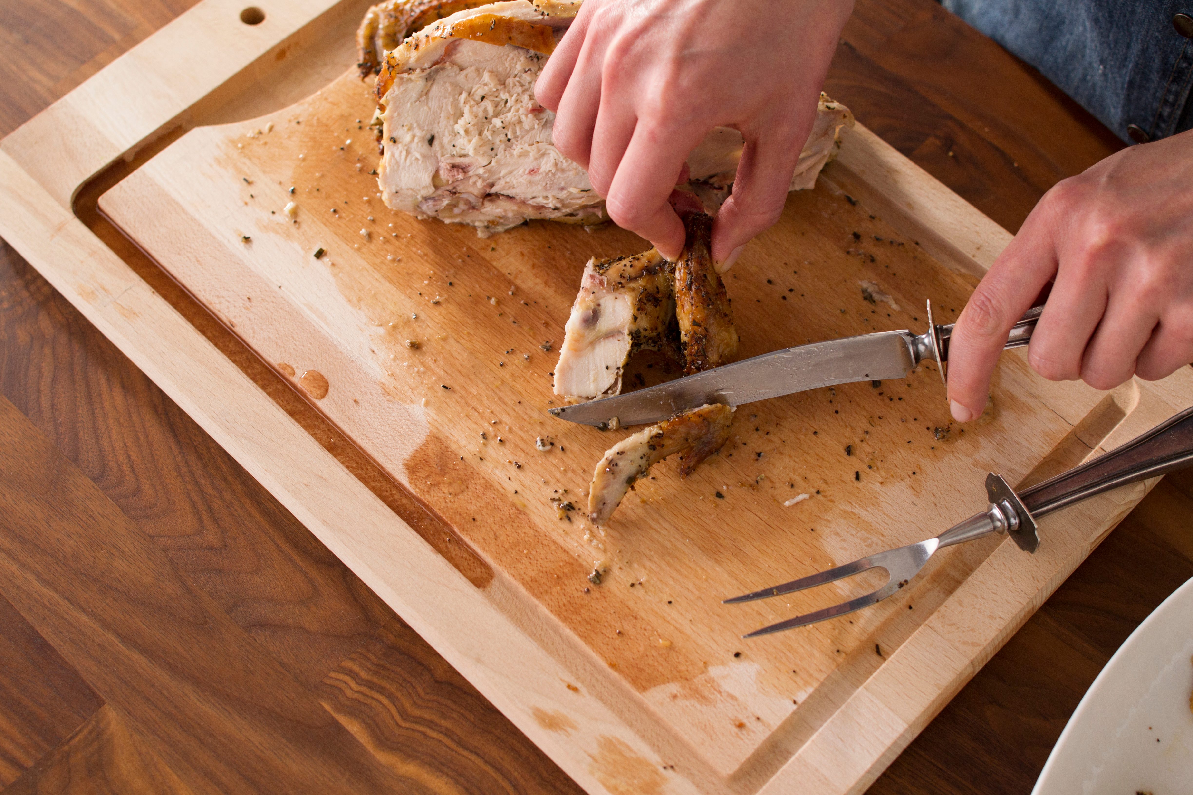 Person slicing the meat from chicken wings on a wooden cutting board