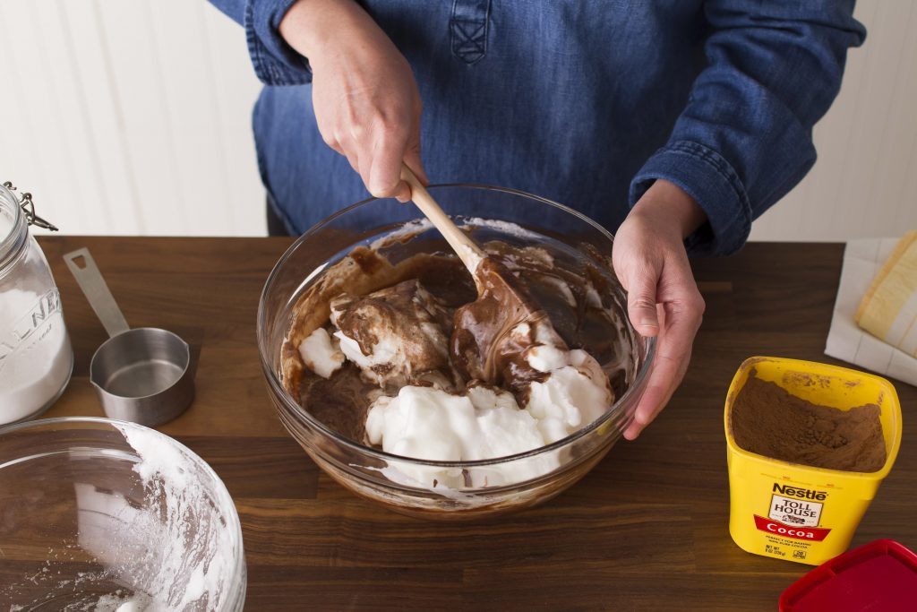 Person using a spatula to fold together chocolate and cream and rotating as they go