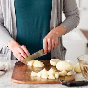 Person using a knife to chop peeled potatoes into cubes