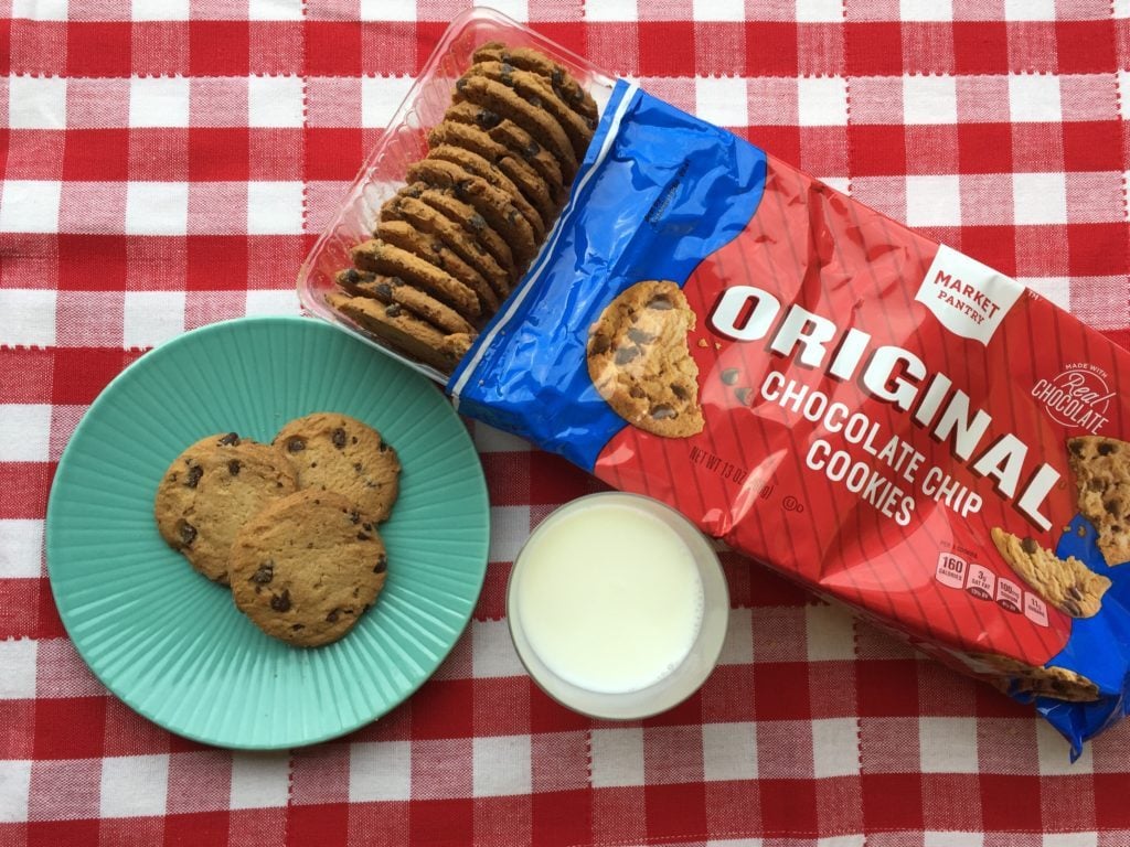 Package of opened Market Pantry chocolate chip cookies with several out and on a blue plate also with a glass of milk nearby