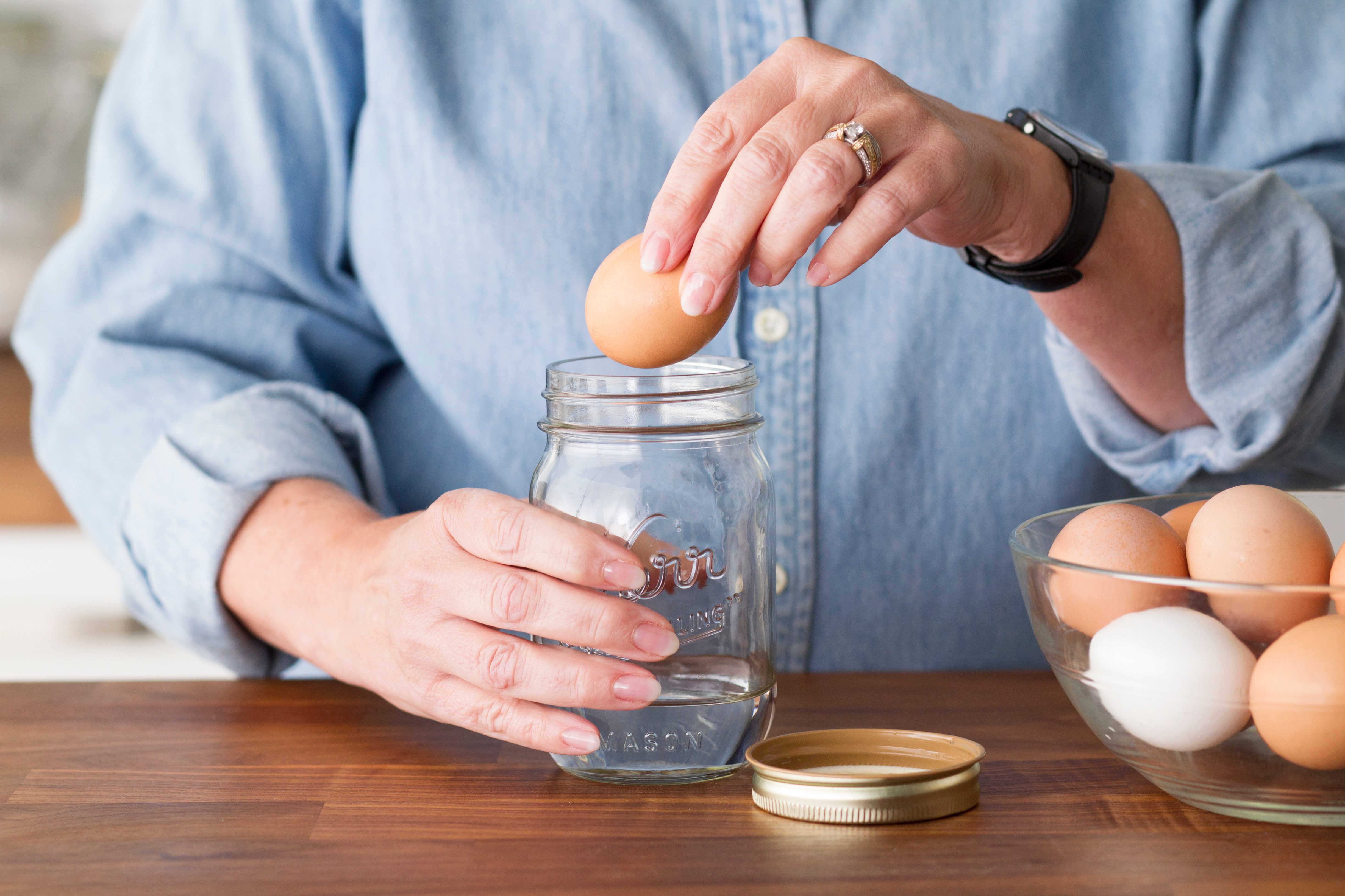 Person lowering an egg into a mason jar with an inch of water