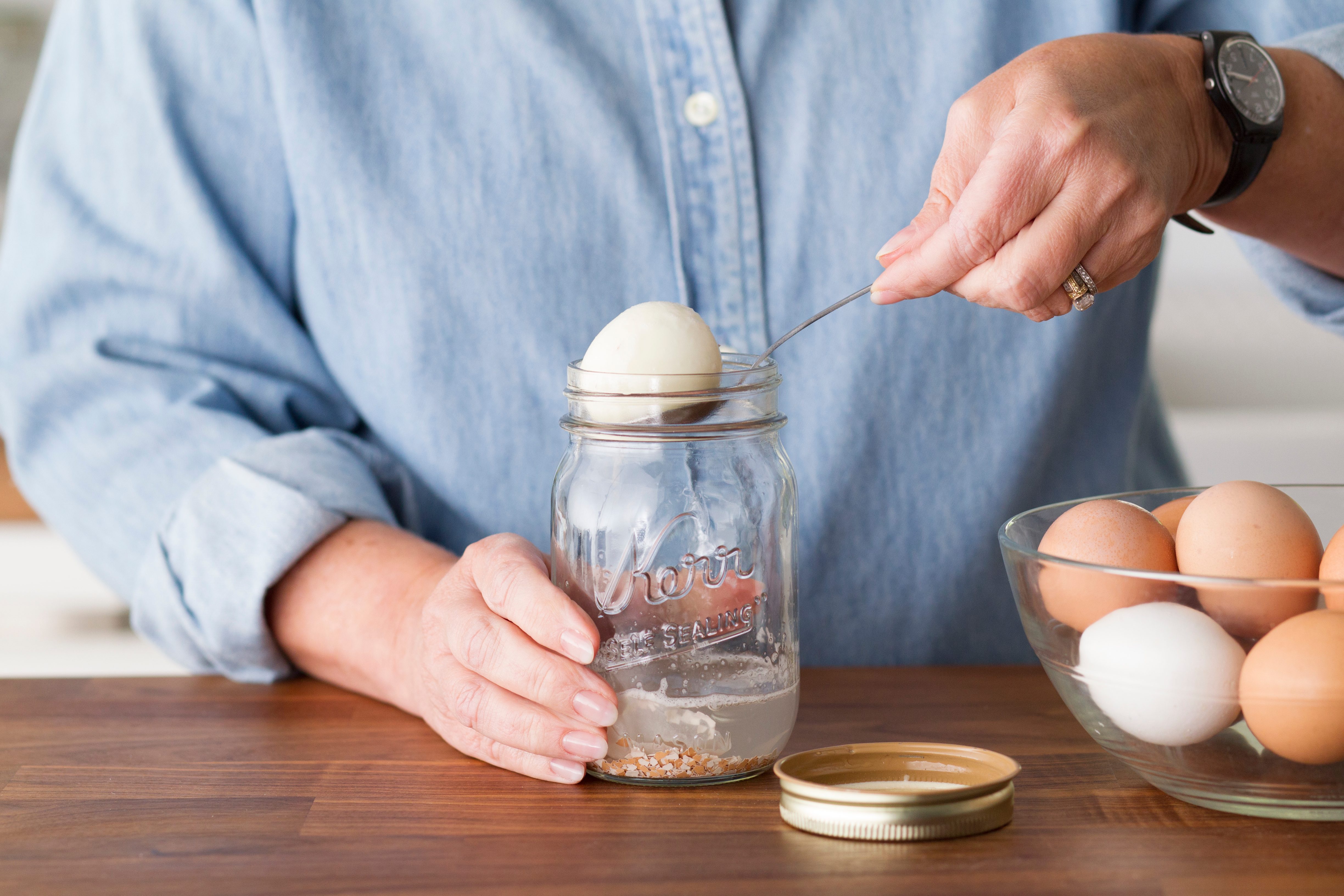 Using a spoon to remove a peeled egg from a mason jar with an inch of water