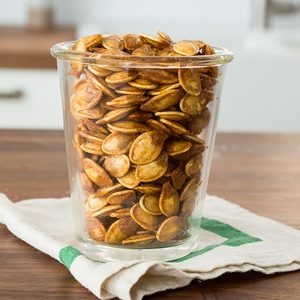 Roasted pumpkin seeds in a glass cup sitting on a wooden table