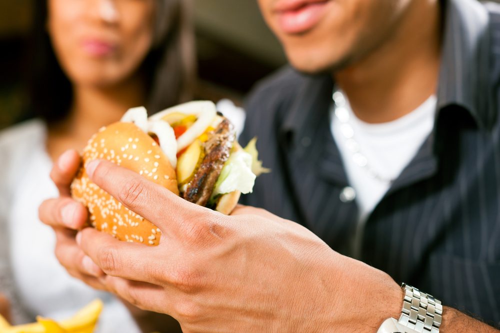 Happy man in a fast food restaurant eating a hamburger with his girlfriend