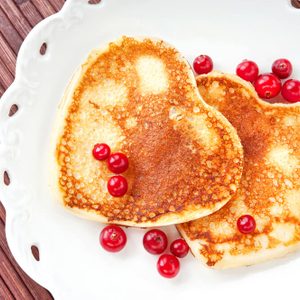 Homemade Heart shaped pancakes with cranberries on white porcelain plate