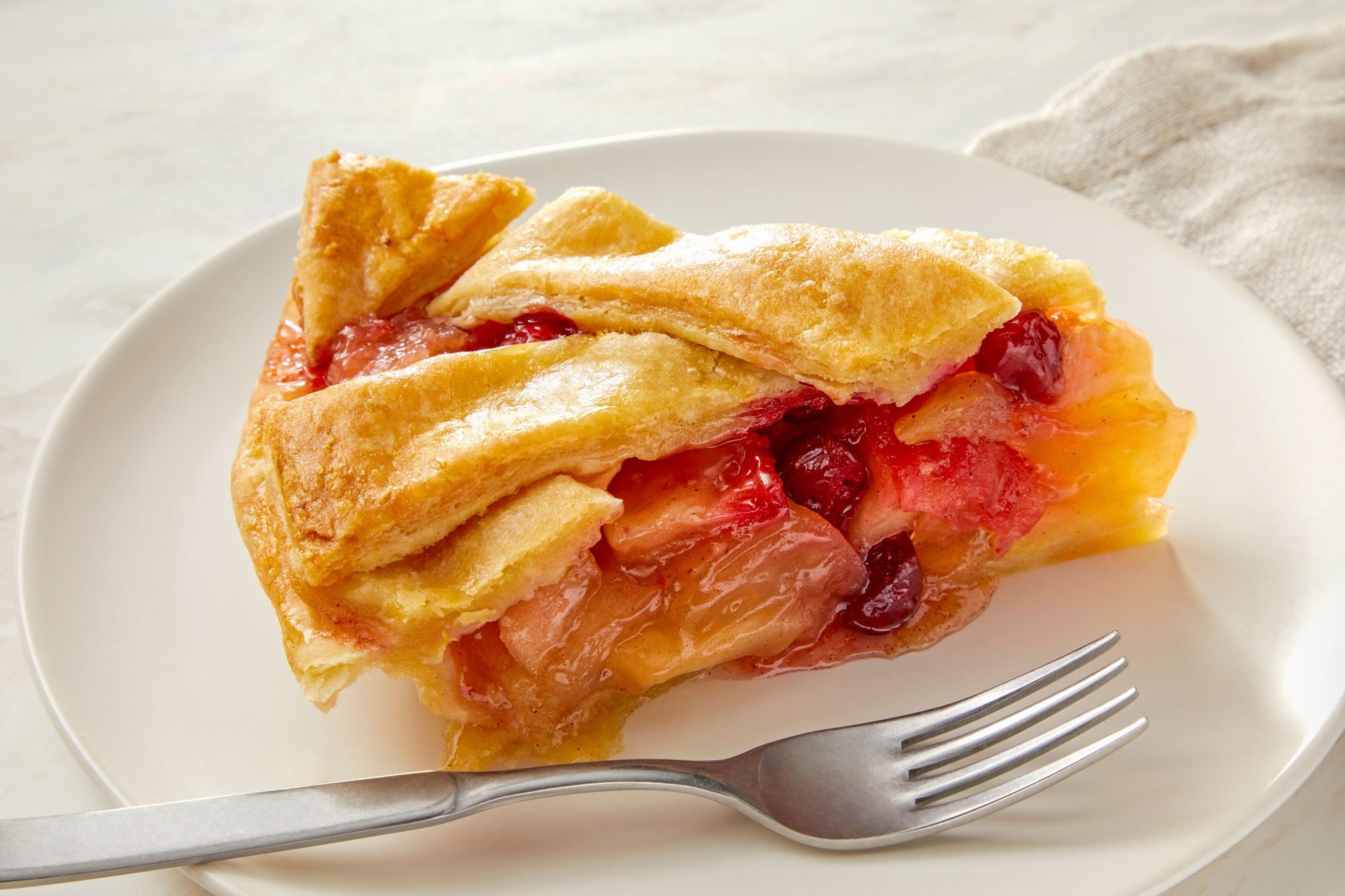 3/4th View Shot of Piece of Cranberry Apple Pie Served on a Plate with a fork; Kitchen Napkin; Marble Background;