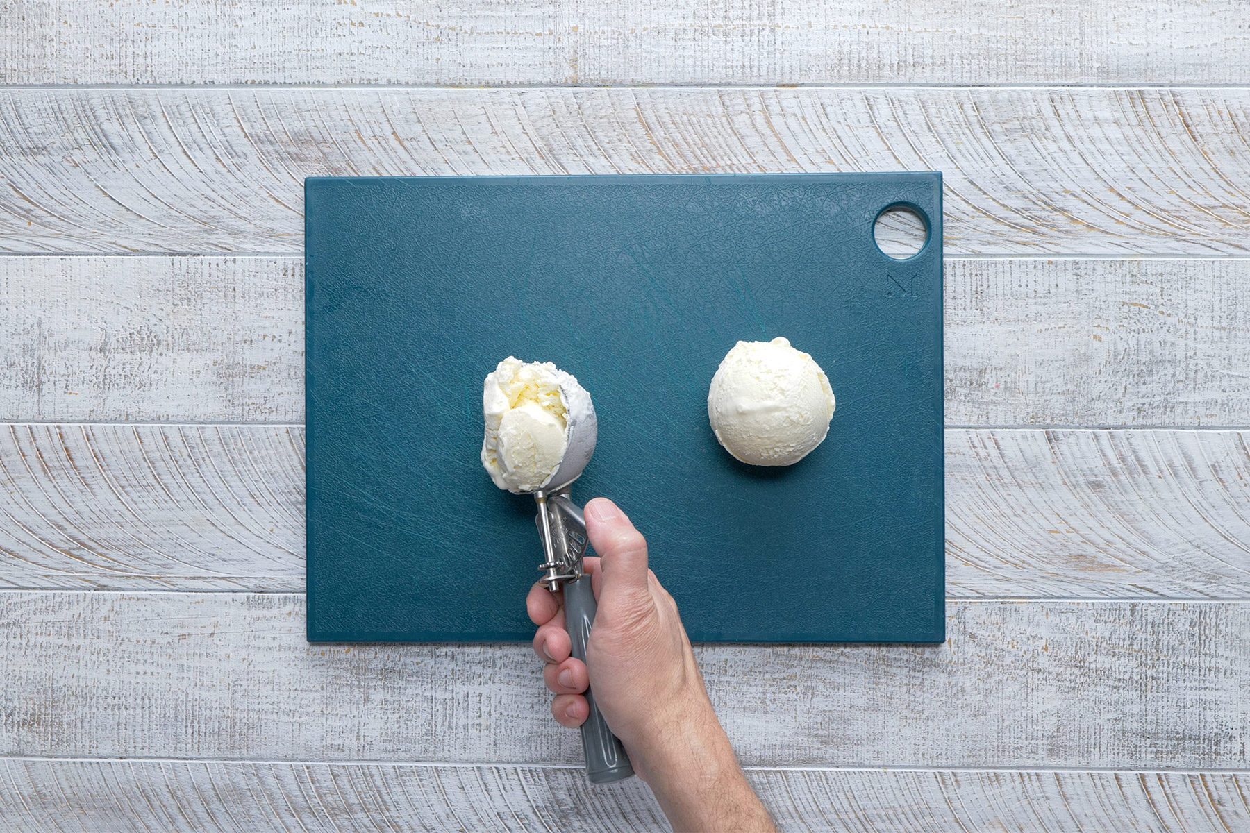 overhead shot; white wooden background; placing two ice cream scoops on a blue board