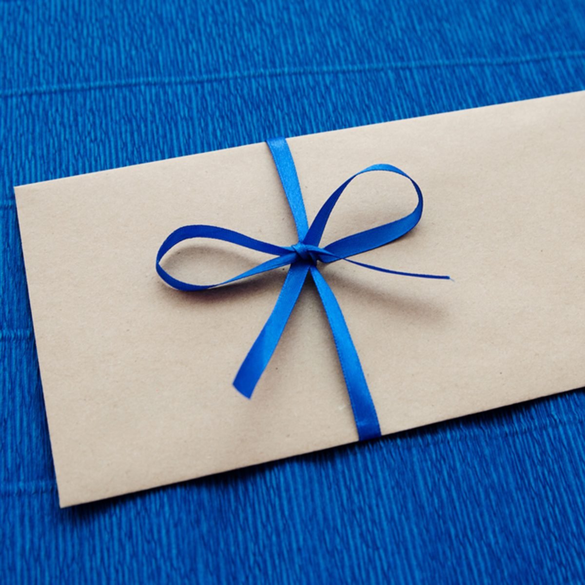 Gift kraft envelope with a blue ribbon on a blue background; Shutterstock ID 517323679