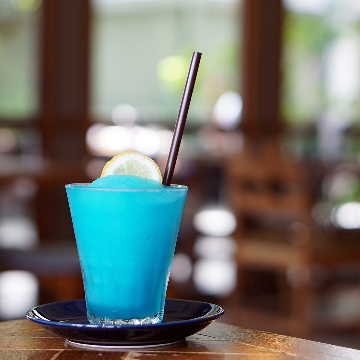 A glass of Frozen margarita cocktail with lime juice, blue grenadine and soda on wooden table and blurred background