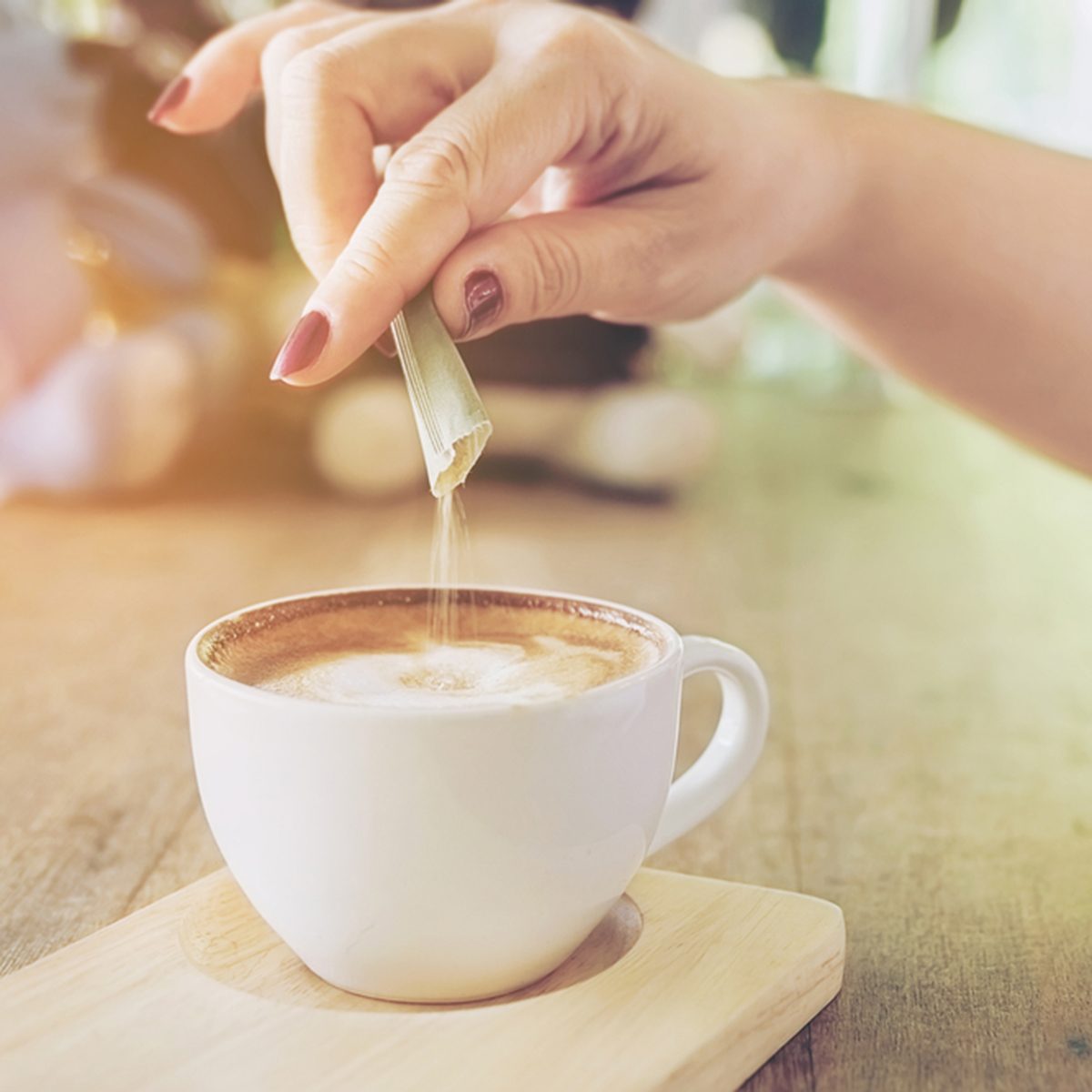 Closeup of lady pouring sugar while preparing hot coffee cup