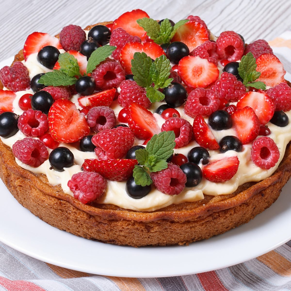 berry tart with fresh strawberries, raspberries, currants, mint and cream close up on the table 