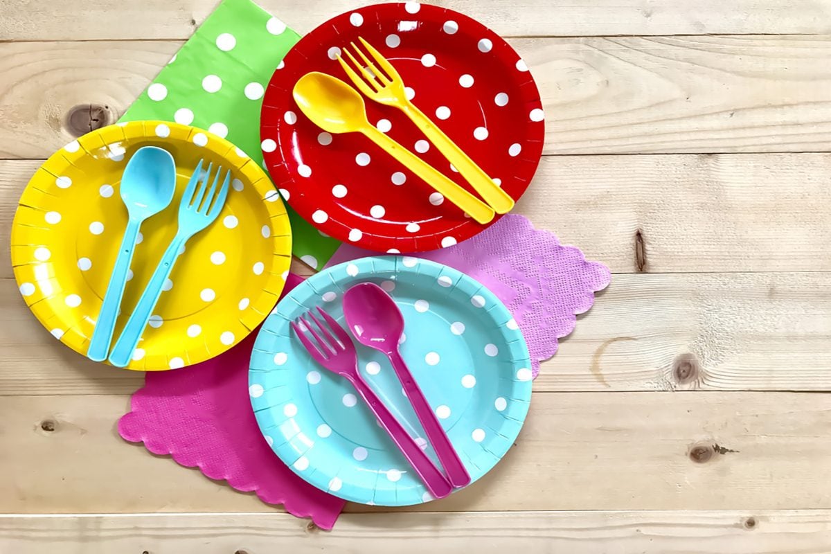 Colorful polka dot paper plate, plastic spoon & fork, napkin on wooden board background.