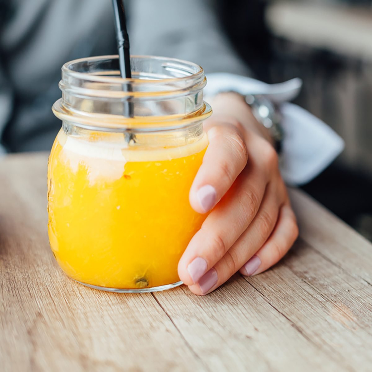 Bottle of freshly squeezed orange. Woman drinking orange juice in a cafe.
