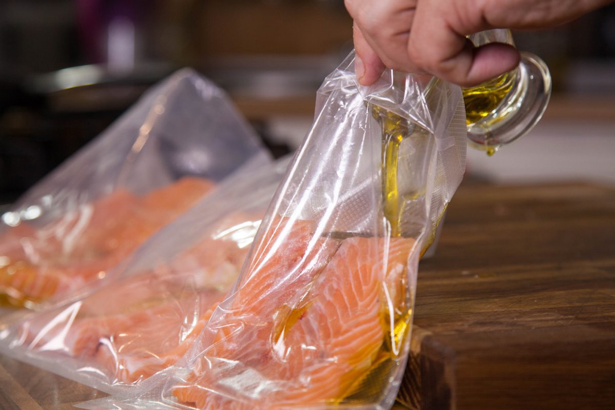 Preparing salmon for sous-vide cooking and pouring olive oil in vacuumed bag.