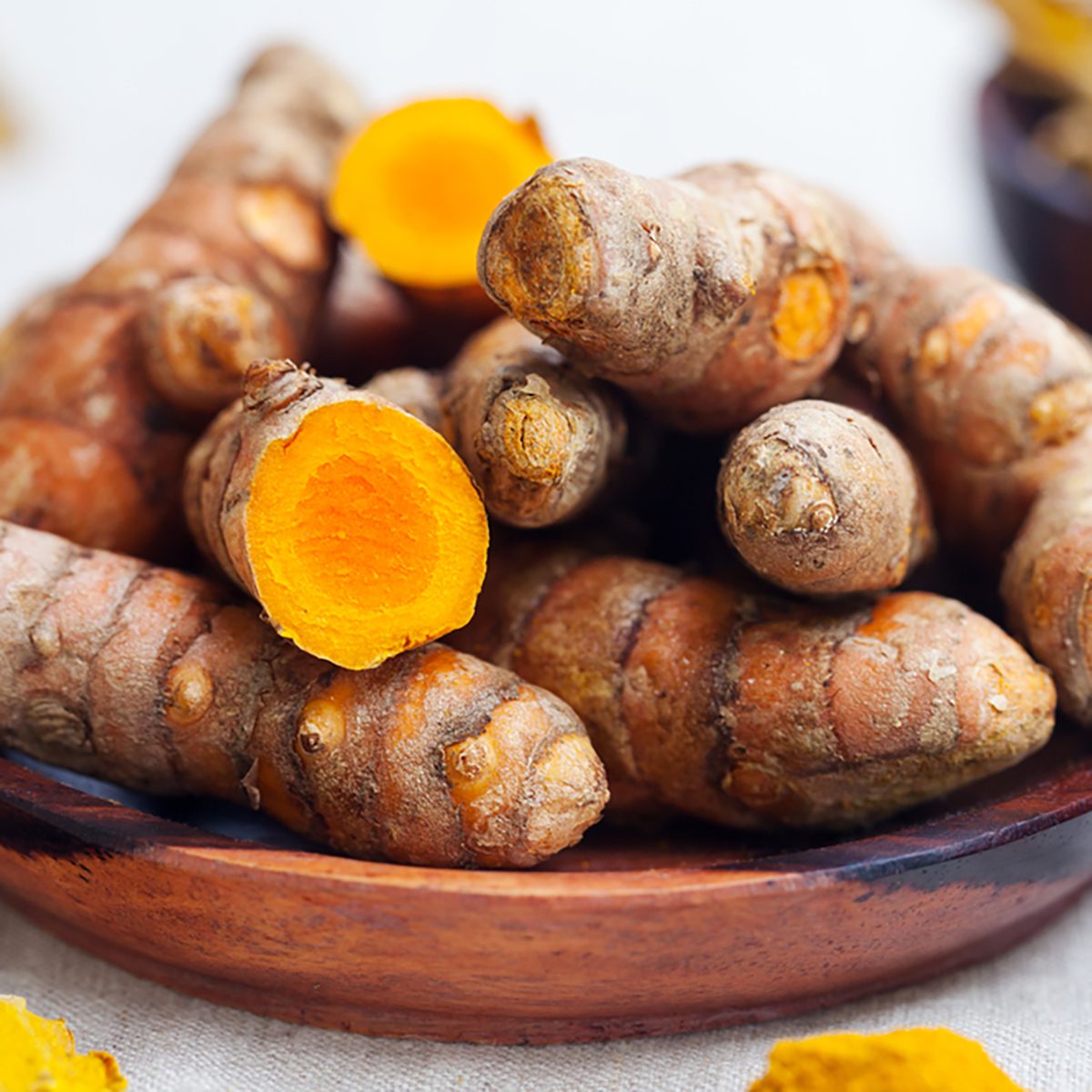 Fresh and dried turmeric roots in a wooden bowl. Grey textile background.