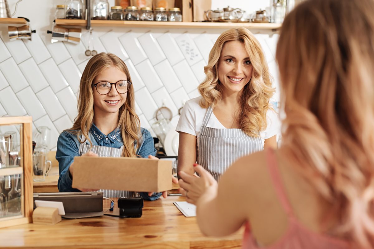 Pleasant baristas selling a box of cookies to the customer.