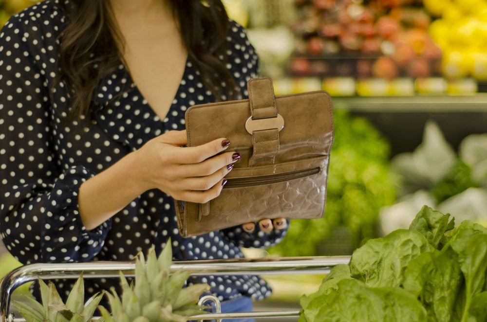 Young woman opening wallet at the supermarket; Shutterstock ID 100487089