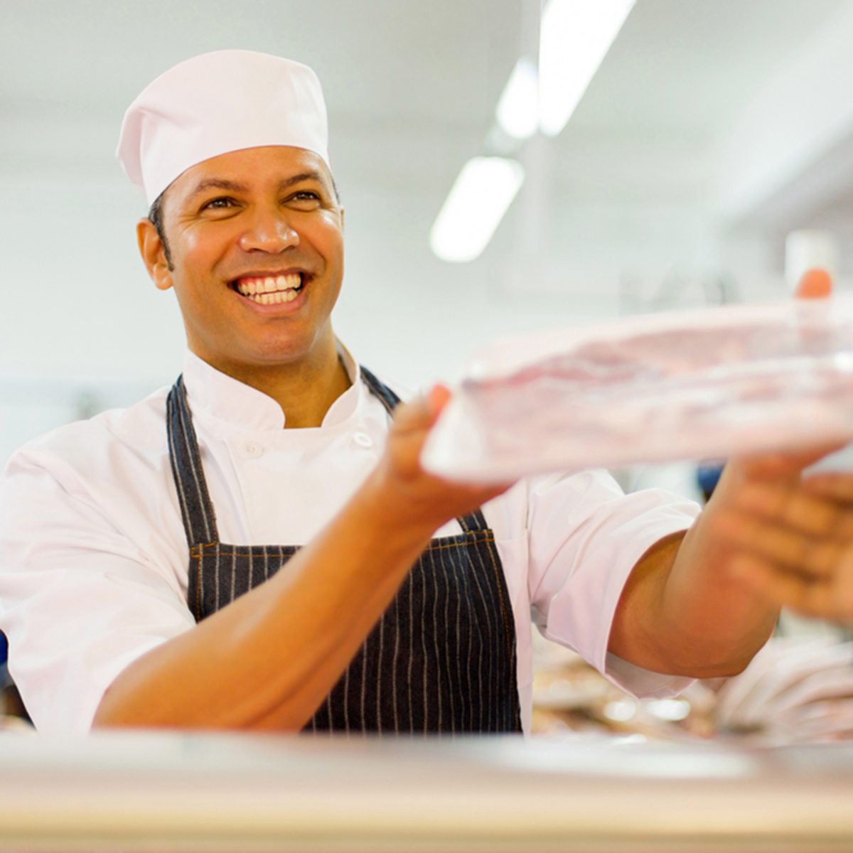 friendly male butcher selling packed meat to customer in butchery