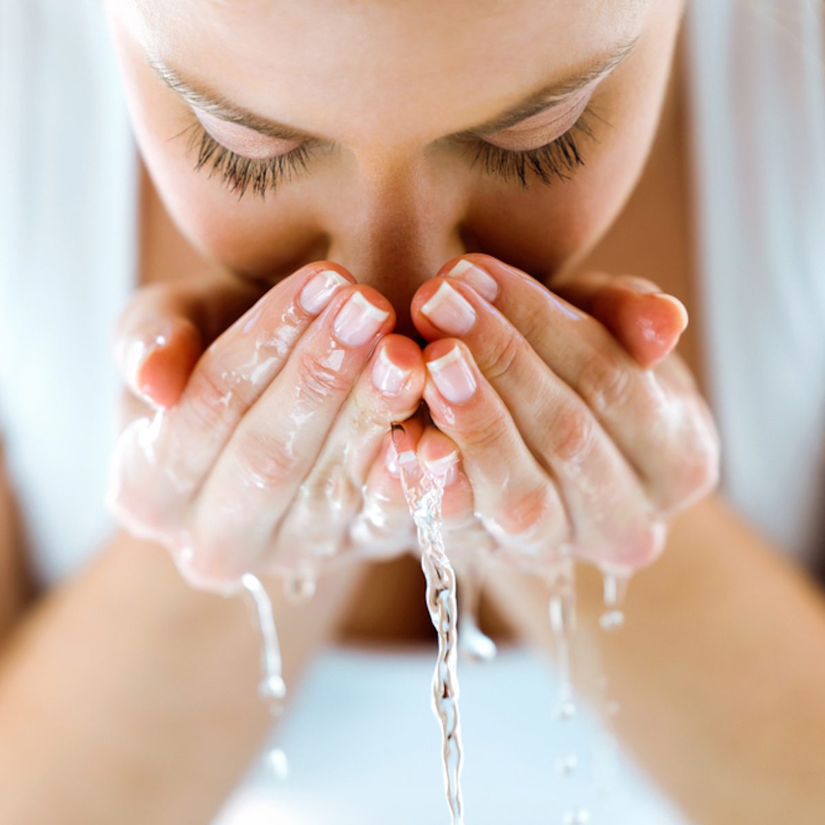 Portrait of beautiful young woman washing her face splashing water in a home bathroom.