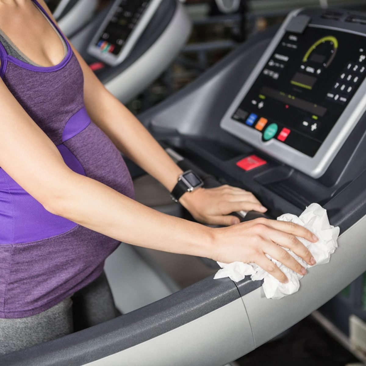 Mid section of pregnant woman cleaning treadmill at the gym