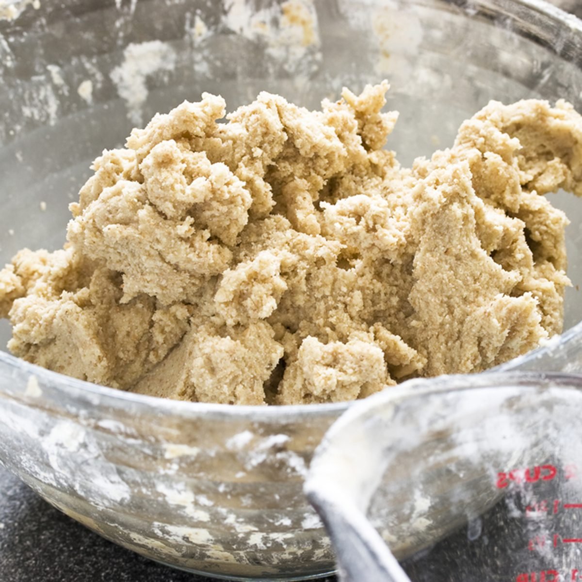 Sugar cookie dough in a glass bowl with measuring cup in front