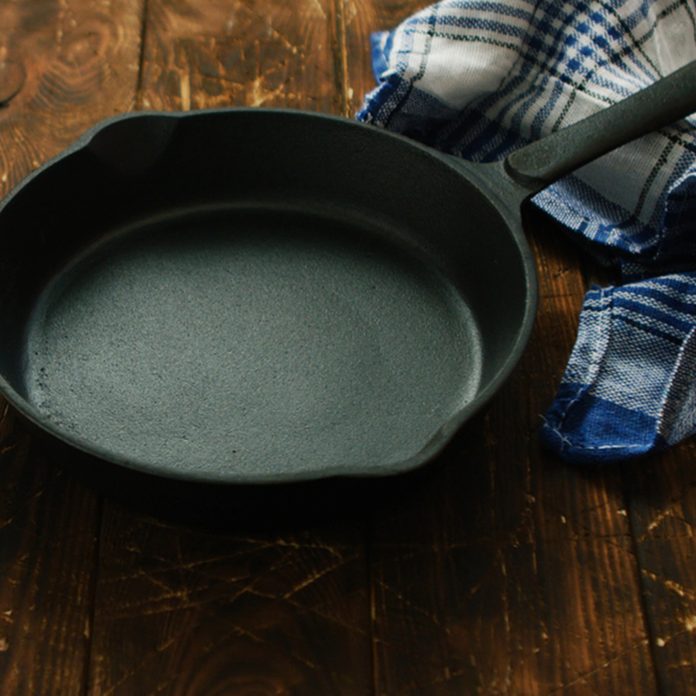 Simple black colored cast iron pan with checkered towel on wooden shabby table surface