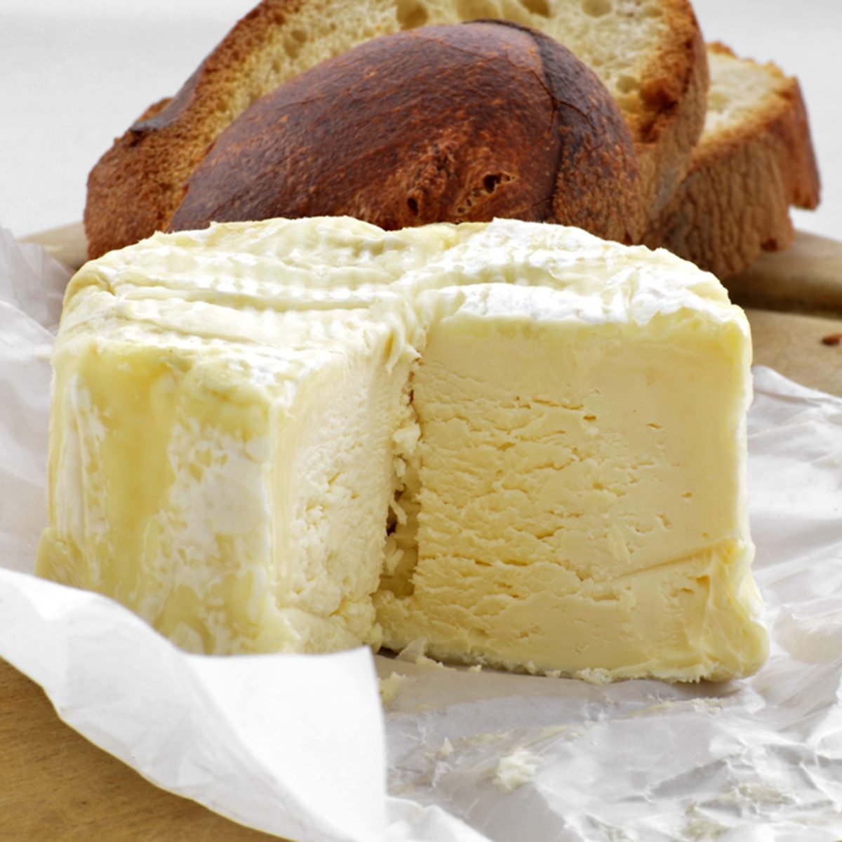 Brillat Savarin soft french cheese in waxed paper on a board with slices of rustic french bread