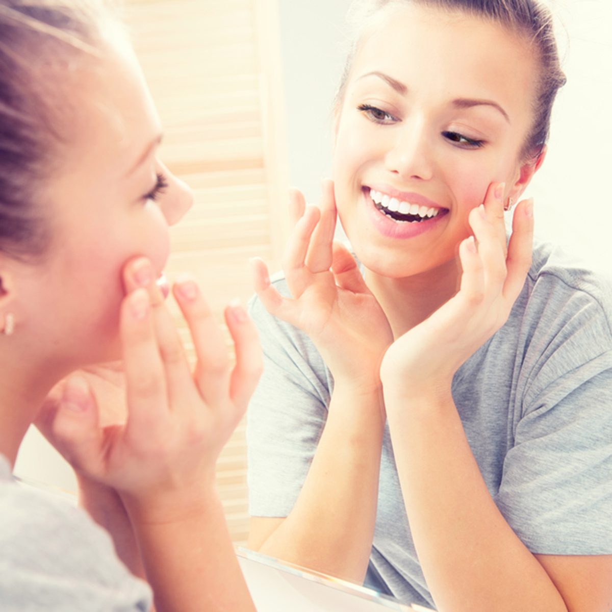 Young beautiful teenage girl touching her face before the mirror