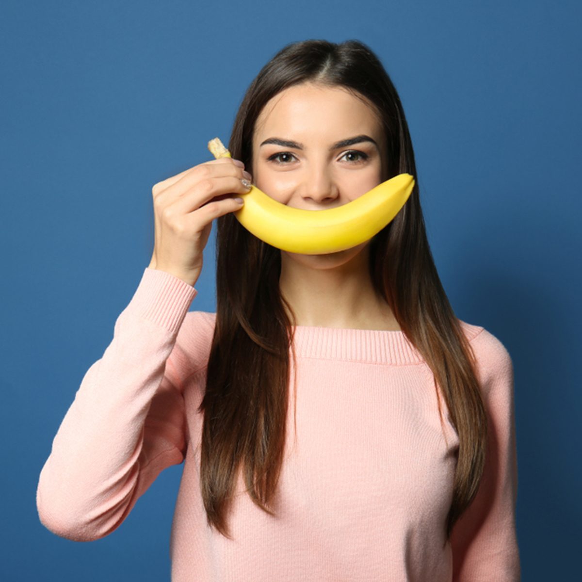Funny portrait of young woman with banana on color background