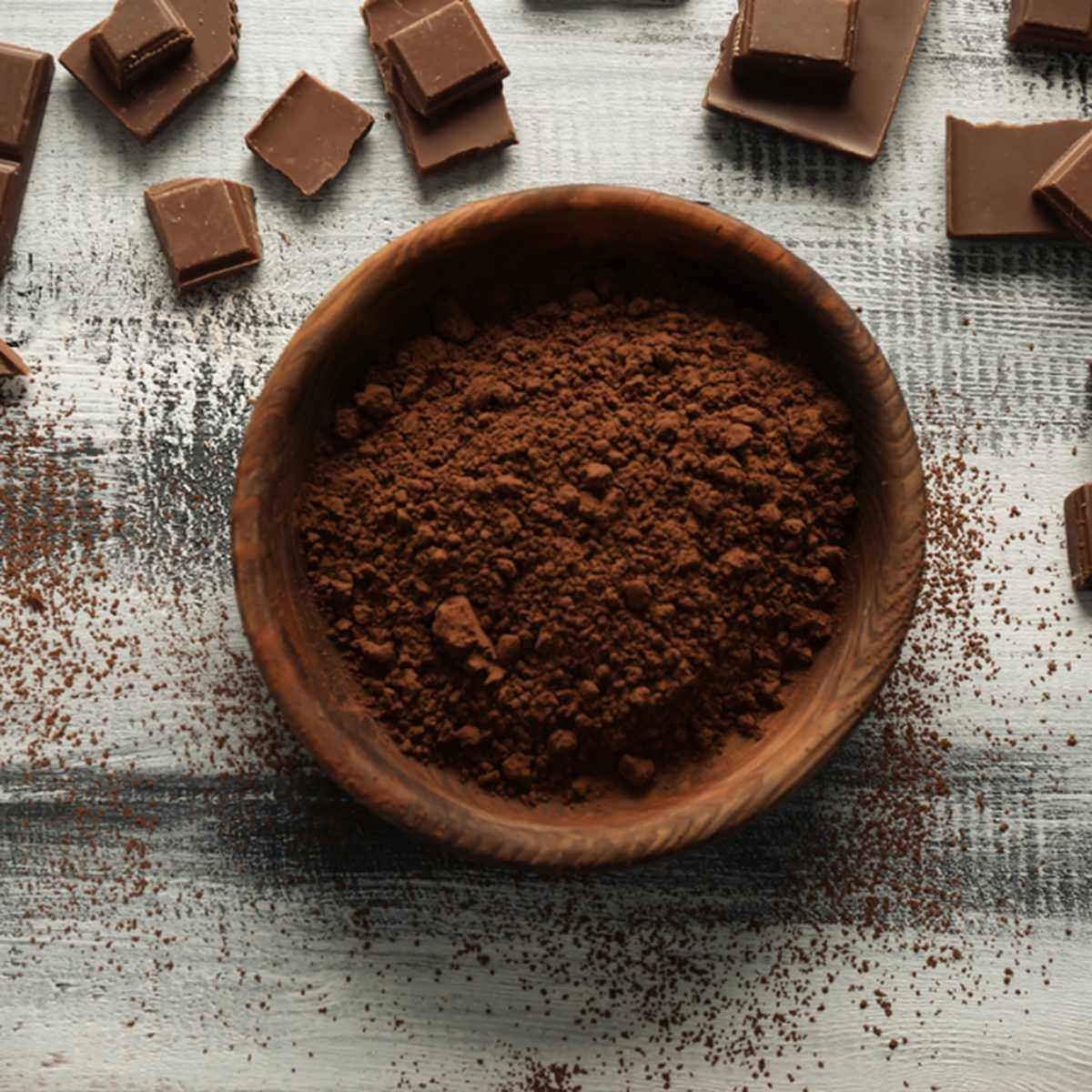 Bowl with cocoa powder and tasty chocolate on wooden background