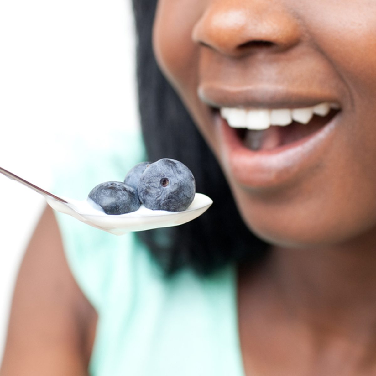 Close-up of a woman eating a yogurt with blueberries against a white background