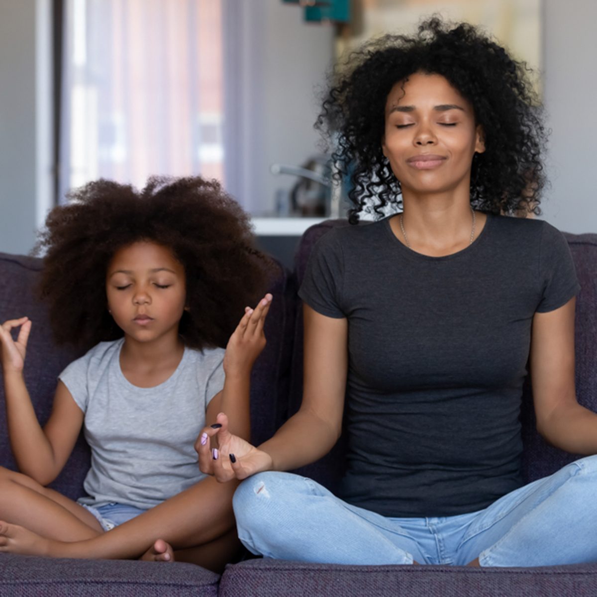 Mindful african mom with cute funny kid daughter doing yoga exercise at home