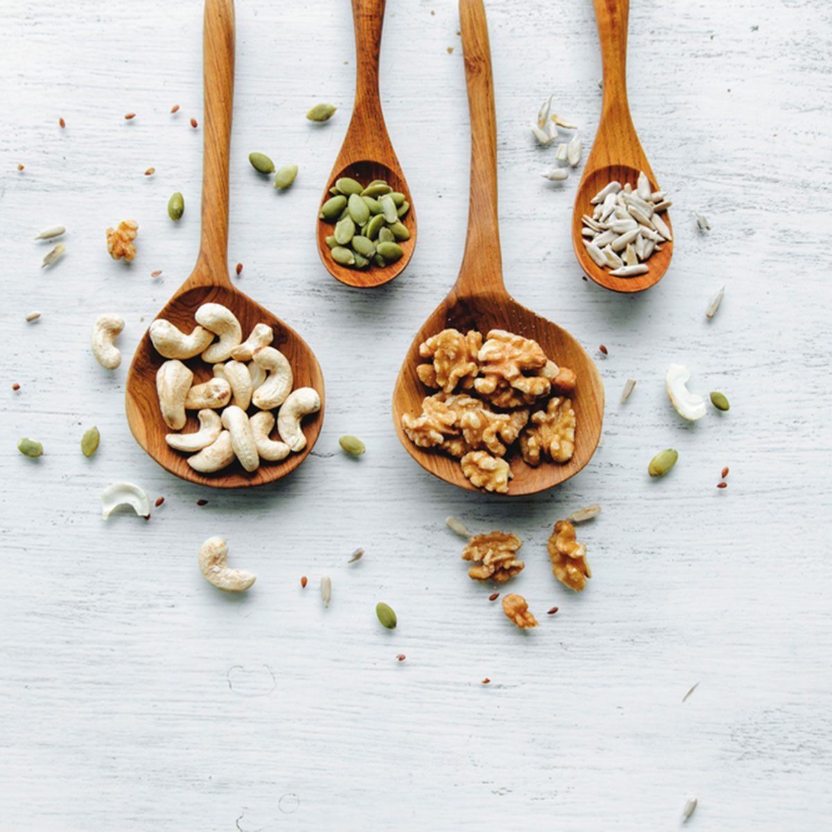 Four wooden spoons with seeds and nuts on the white table