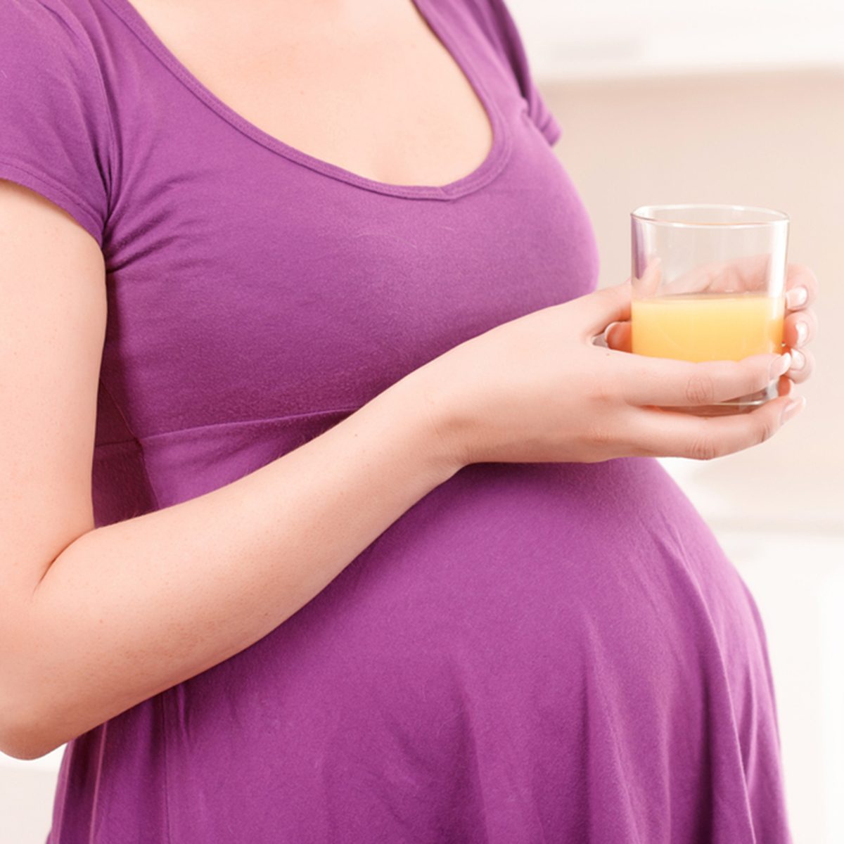 Close up portrait of pregnant woman holding glass filled with orange juice.