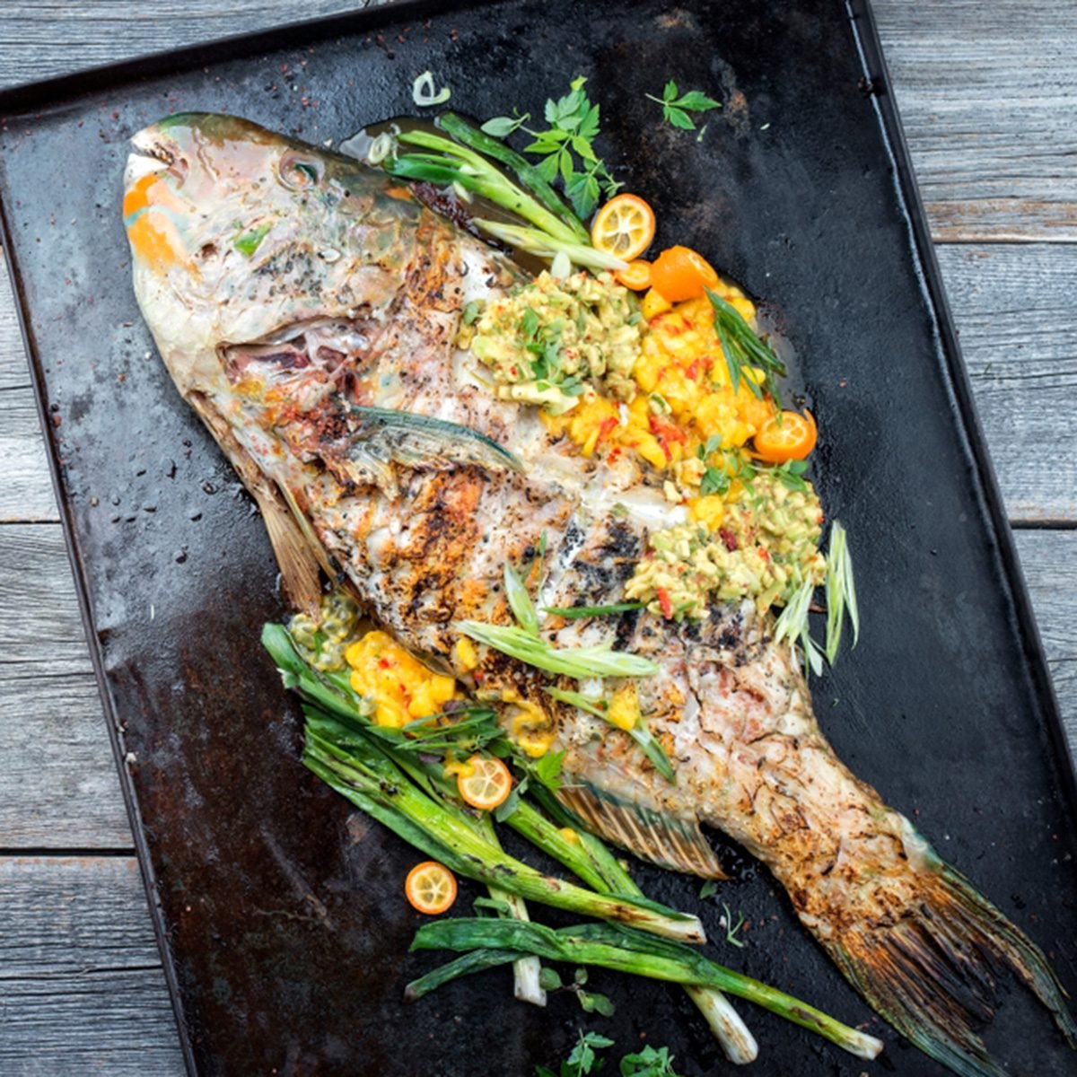 Traditional BBQ parrotfish with mango salsa as top view on a black board