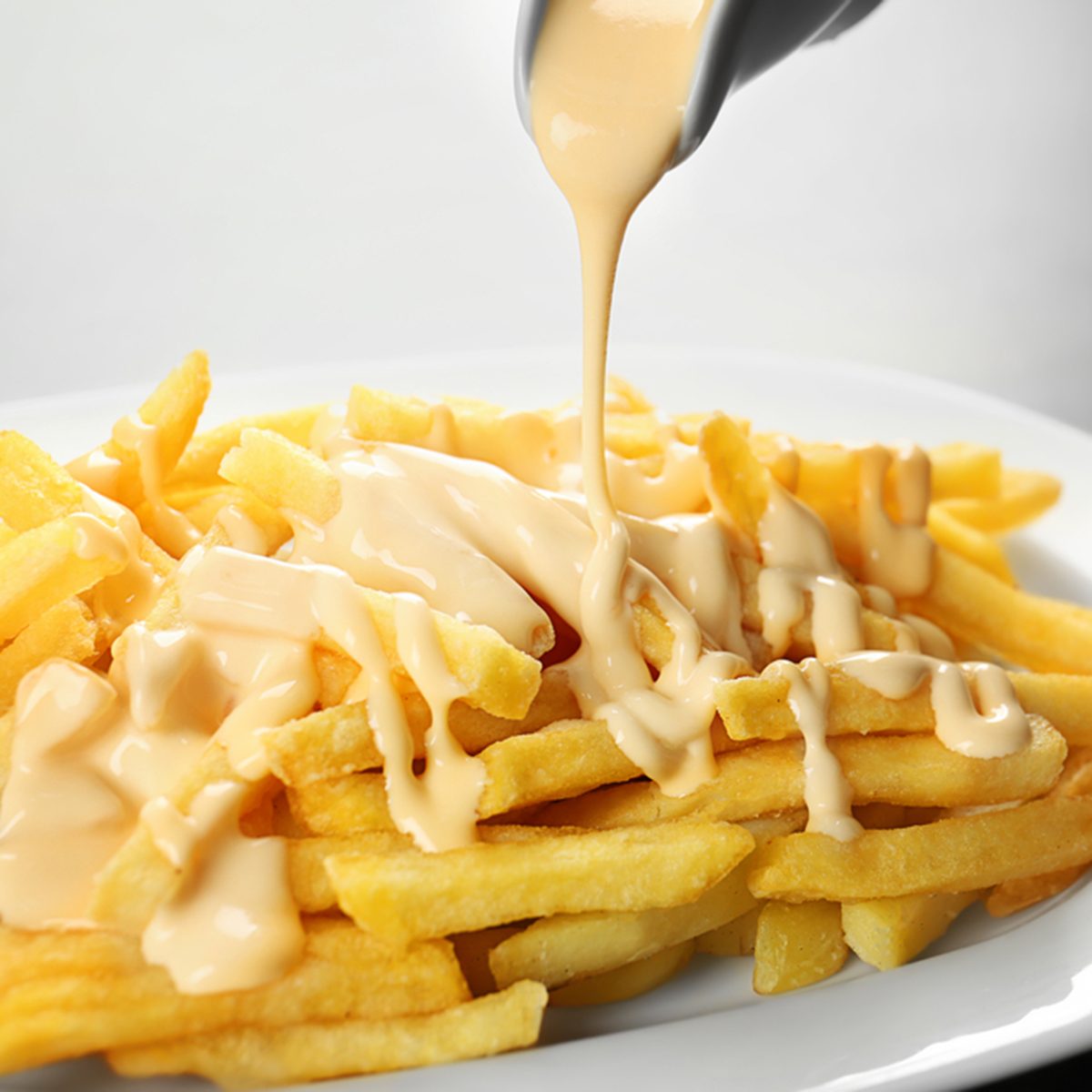 Pouring cheese sauce on french fries, closeup