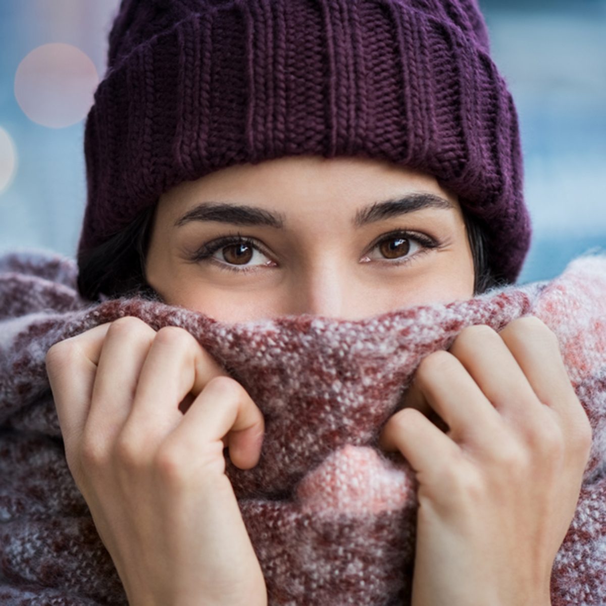 Winter portrait of young beautiful woman covering face with woolen scarf.