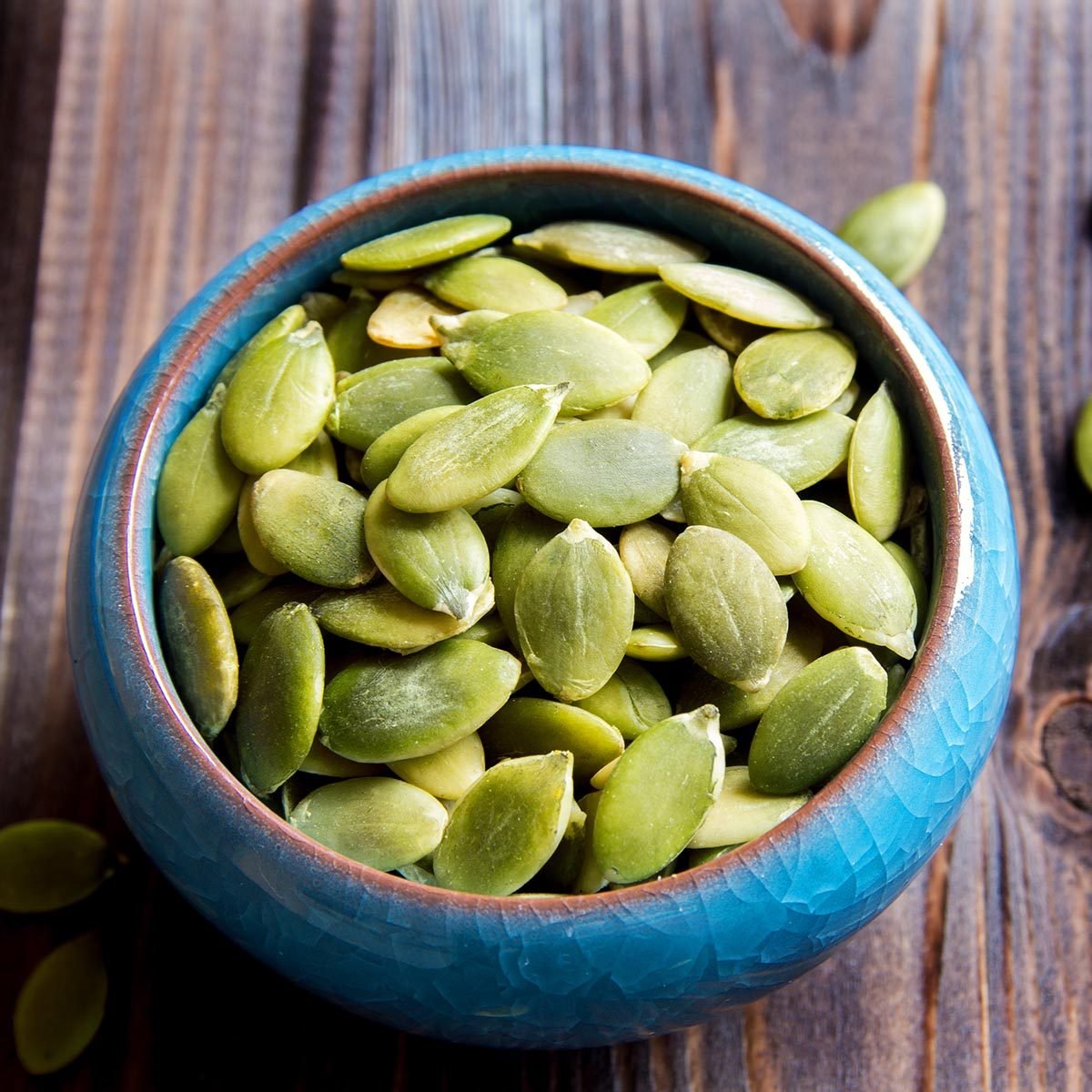 Pumpkin seeds in blue bowl over wooden background close up