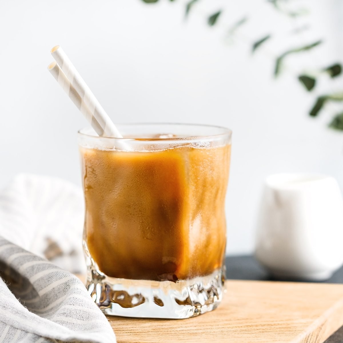 Refreshing iced latte coffee in a glass with straws in a modern kitchen.