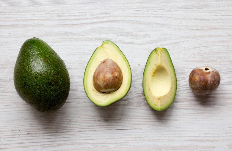 Whole and chopped avocados on white wooden background, overhead view. Top view, from above, flat lay.