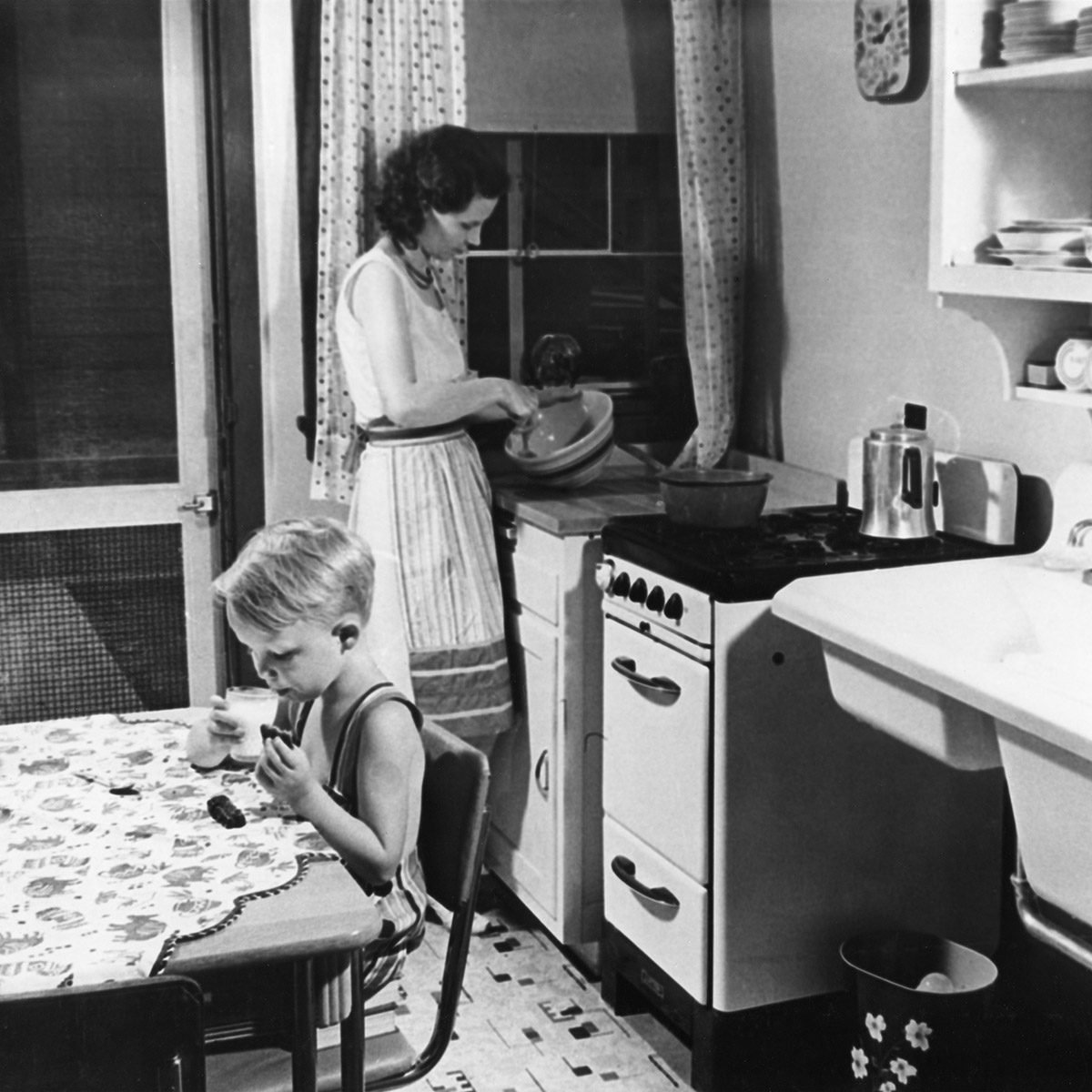 Woman Cooking in Kitchen with Young Boy Eating Cookies with Milk