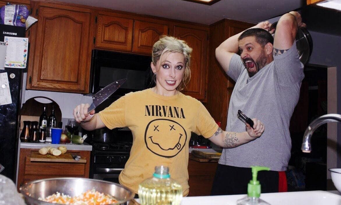 Adult brother and sister messing around in the kitchen with knives and a chair