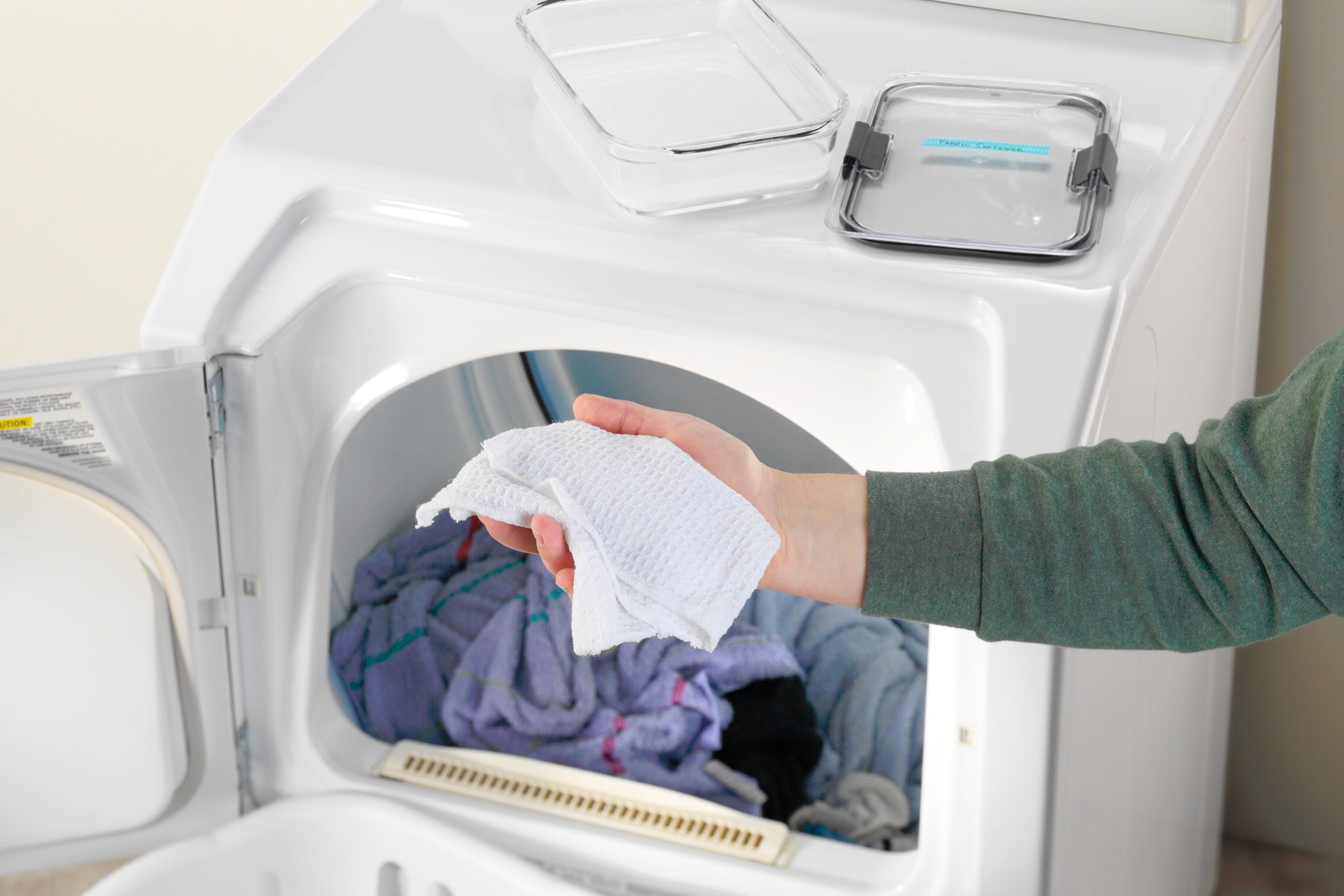 hand holding Homemade Dryer Sheet in front of an open dryer with items inside