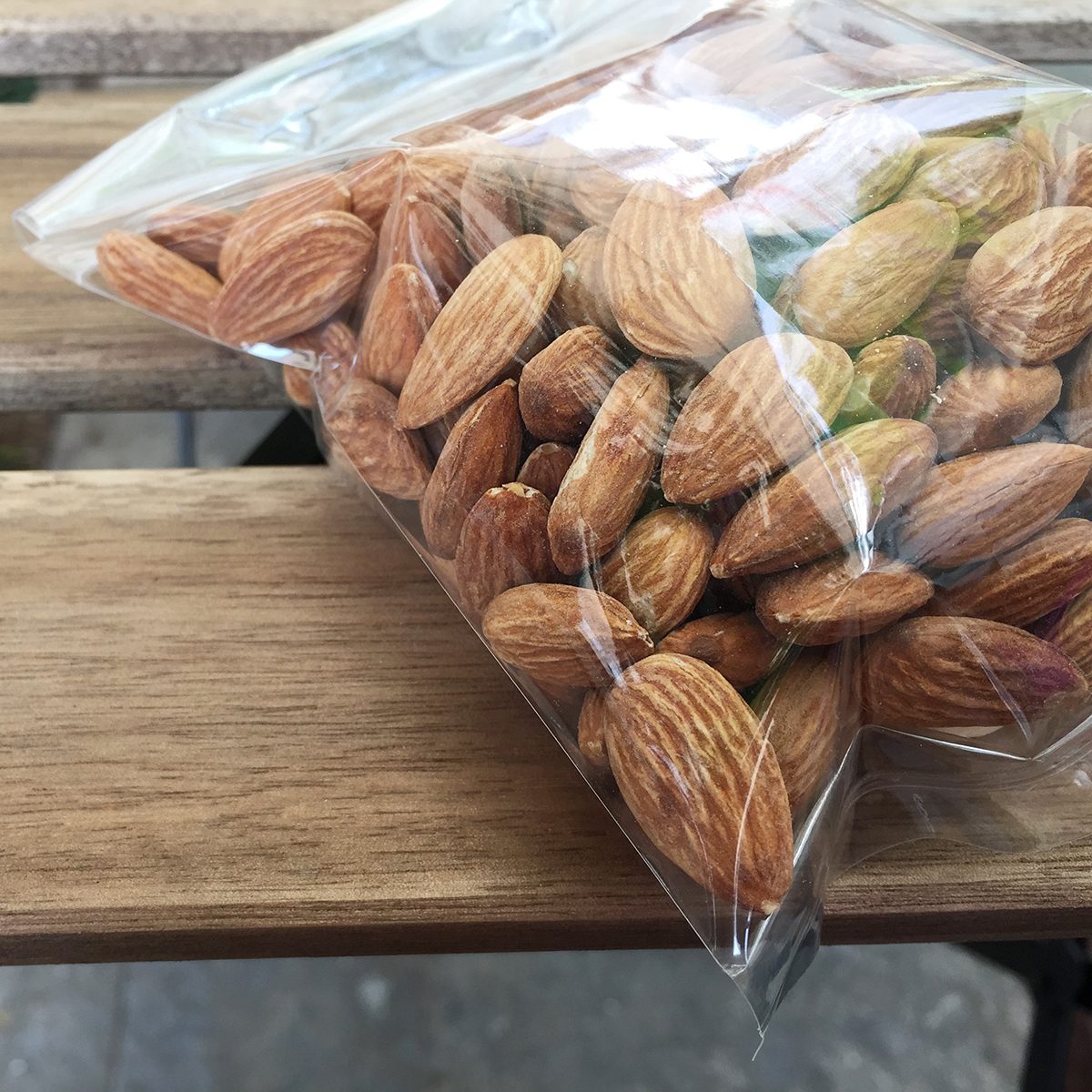 Almond nuts in plastic bag on wood background;
