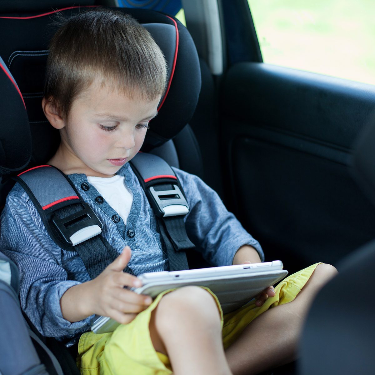 Cute boy, playing on tablet in the car