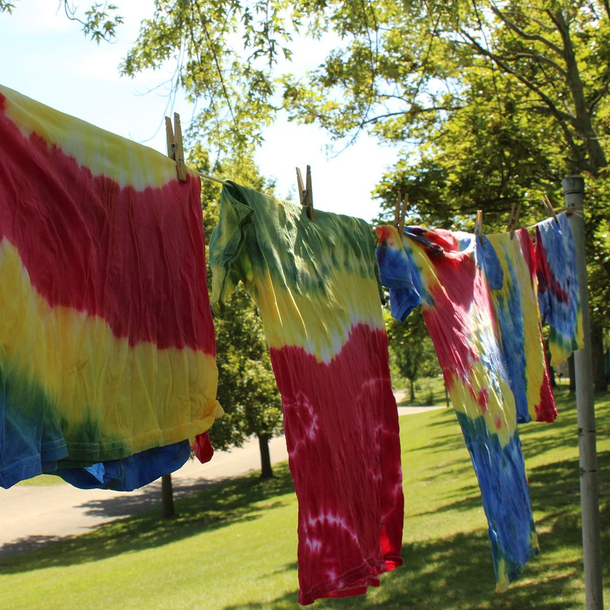 Multi colored tie dye tee shirts hanging on clothesline with trees