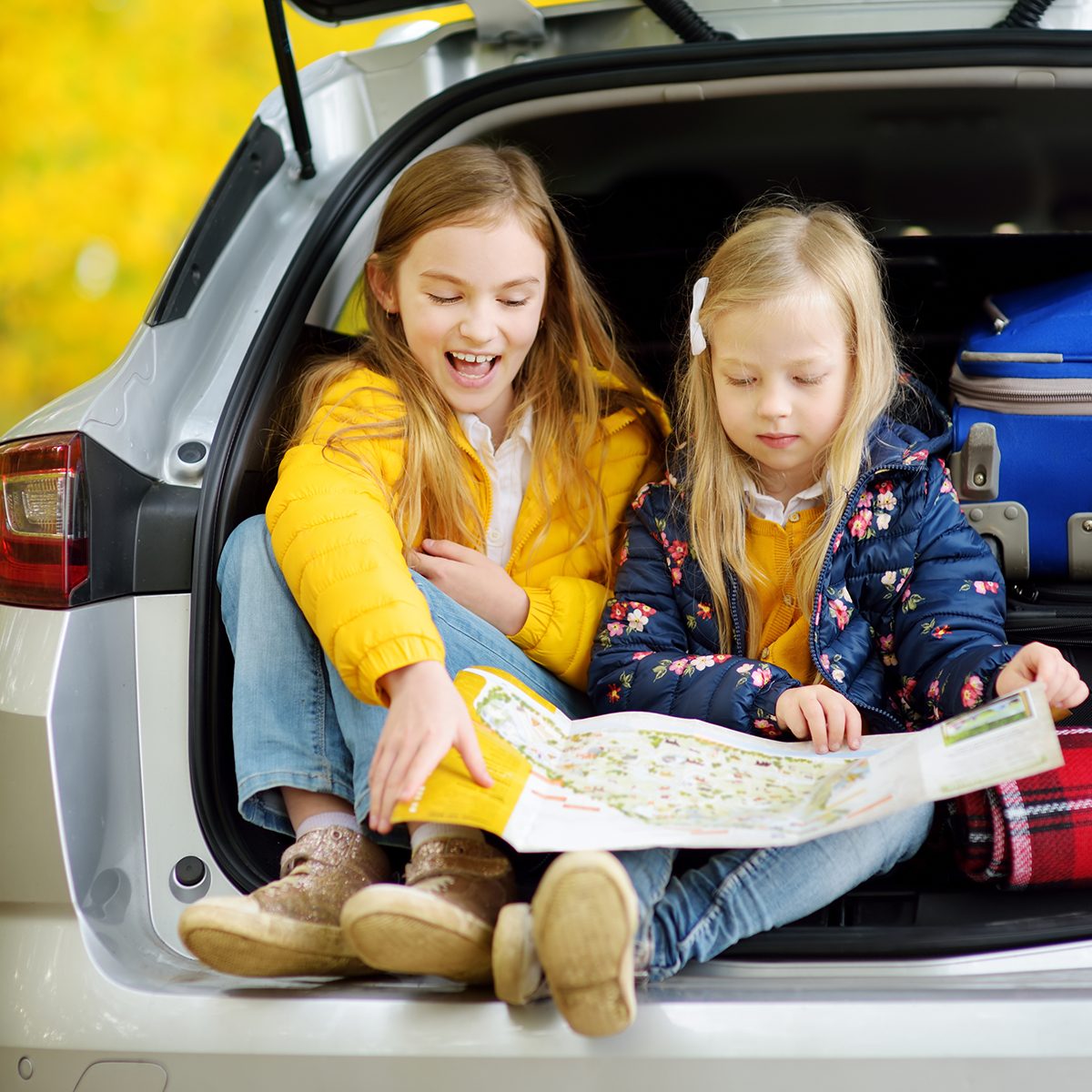 Two adorable girls sitting in a car trunk before going on vacations with their parents.