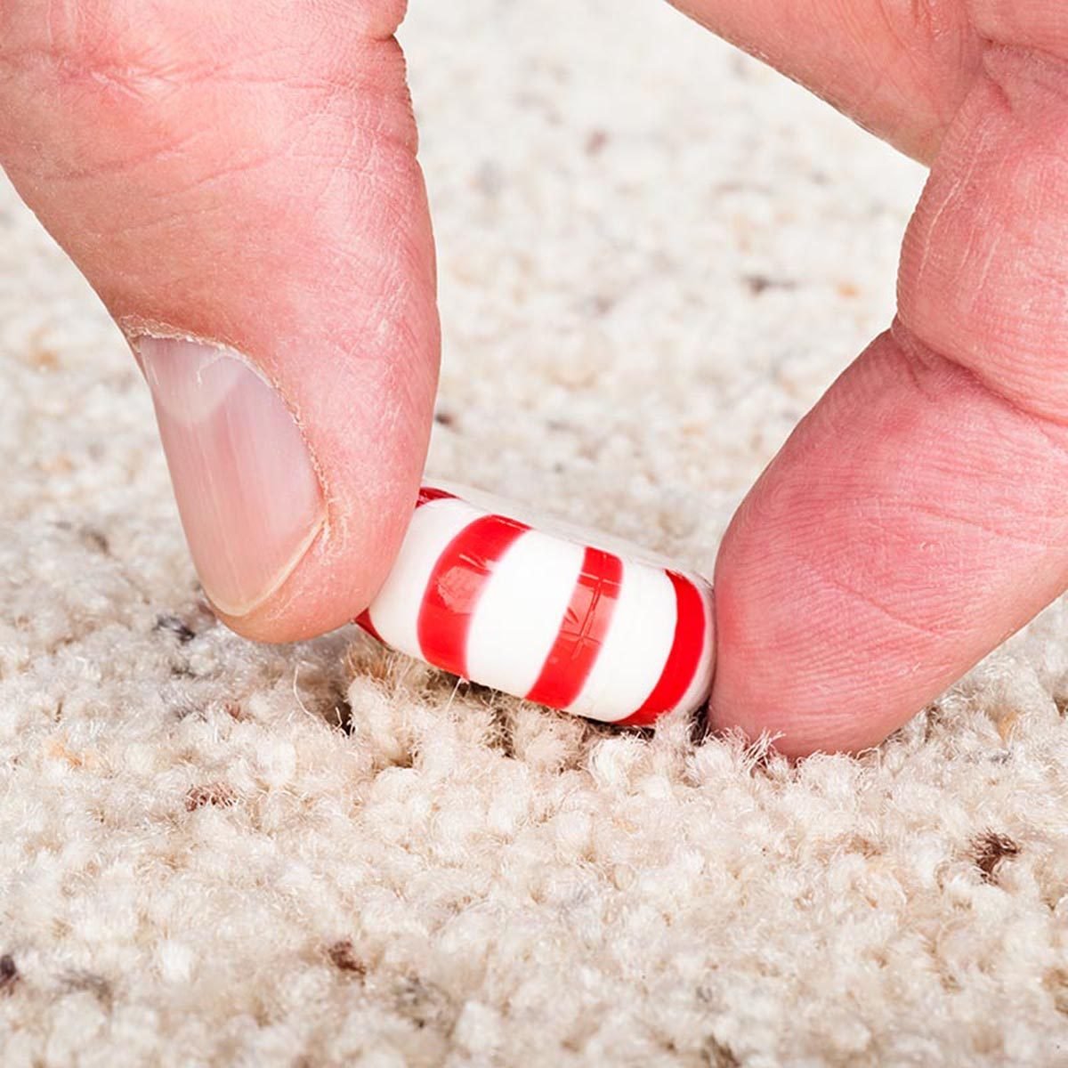 A person pulling a sticky candy mint off the carpet.