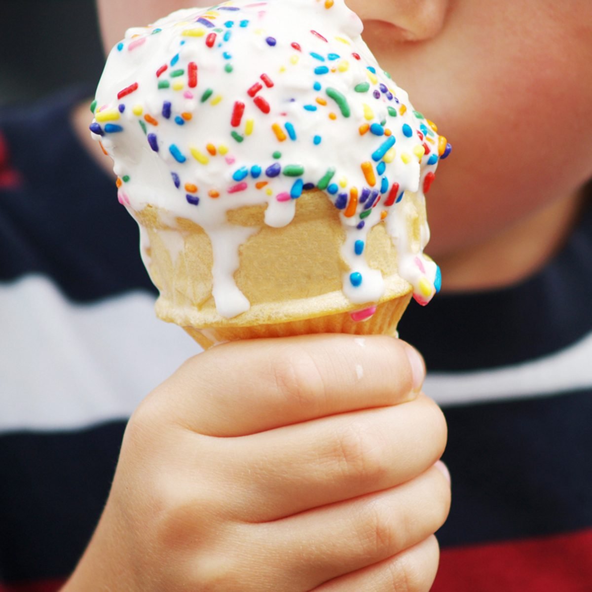 a young child's hand holding a dripping ice cream cone with colorful sprinkles